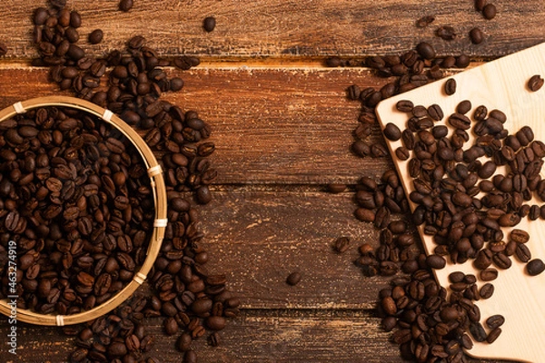 Fototapeta A basket of coffee beans at the side of image, and coffee beans on the wooden board