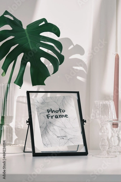 Fototapeta black and golden photo frame , black mirror with color candles , glass lamp , glass flower pot with in white background and daylight , green leaf , home decoration photography