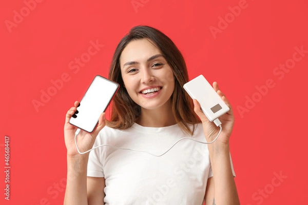 Obraz Young woman with phone and power bank on color background