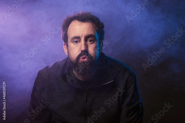 Obraz portrait of attractive man blowing into the camera with colored smoke behind him