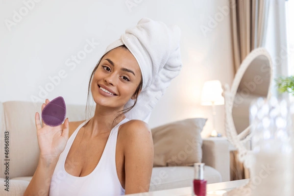 Obraz Young woman washing face with silicone pink brush and cleansing foam. Cosmetic products. Attractive smiling girl using pink silicone cleansing facial brush. 