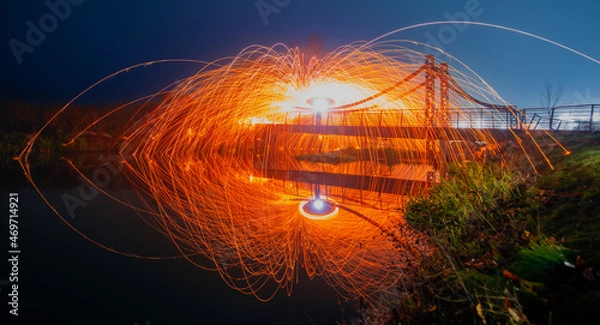 Fototapeta Steel wool sparks reflecting water Long exposure night landscape.