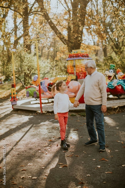 Fototapeta Grandfather having fun with his little granddaughter in the amusement park