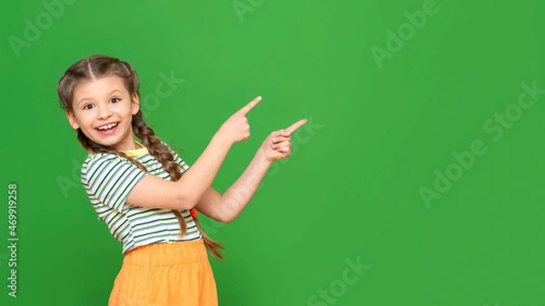 Fototapeta A little girl points with both hands at the advertisement. Copy space. Isolated background.