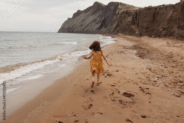 Obraz A child runs along the beach . The girl runs along the shore. A girl in a yellow dress .Yellow clothes.