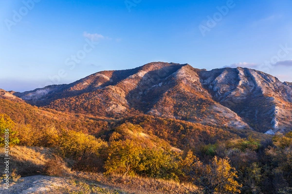 Fototapeta Mountains of white stone covered with autumn forest with yellow leaves illuminated by the sun at sunset from the side. Beautiful play of light and shadow