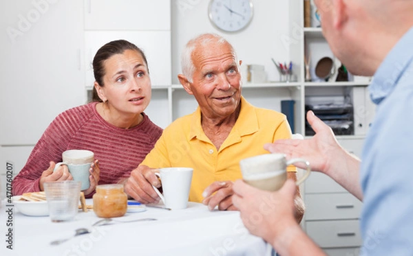 Obraz Smiling father, daughter and son-in-law drinking tea at home. High quality photo