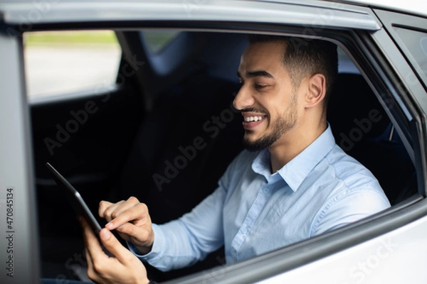 Fototapeta Cheerful middle eastern businessman checking emails while going to airport