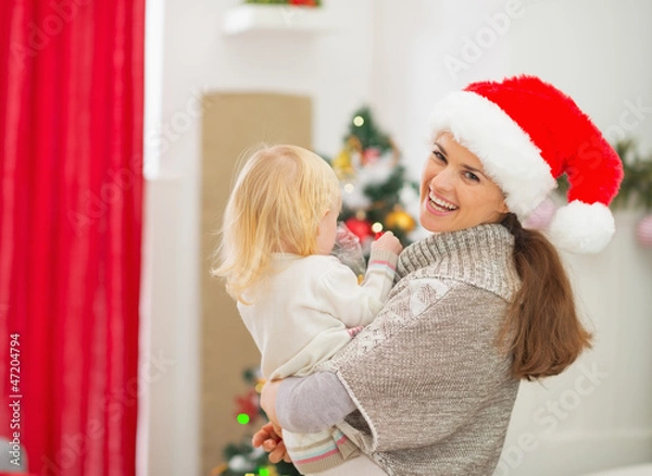 Fototapeta Mother holding baby in front of Christmas tree