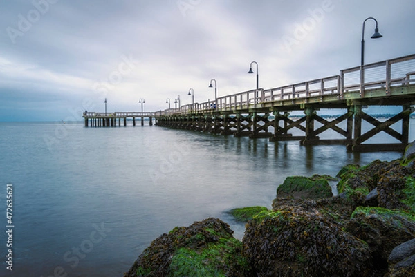 Fototapeta Dramatic seascape with a long commercial pier with lamps and seaweed-covered rocks in New Haven Harbor, Connecticut.