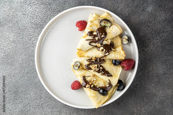 Fototapeta Pancakes with chocolate and berries on a dark background, top view. The concept of the week of pancakes, Russian carnival. Russian pancakes.