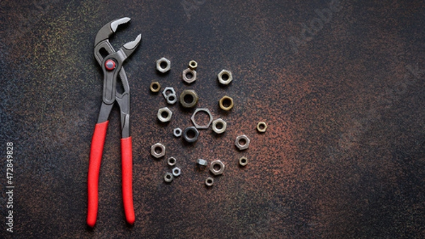 Fototapeta Top view of adjustable universal pliers for repair and assorted nuts on dark rusty background with copy space