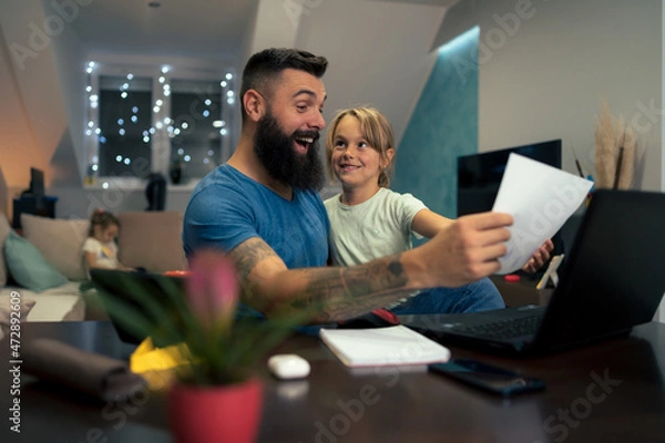 Fototapeta Young businessman working at home while using laptop and his daughter interrupts him