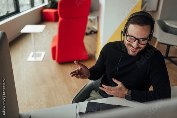 Fototapeta Relaxed caucasian man with glasses, talking to his boss over a video.