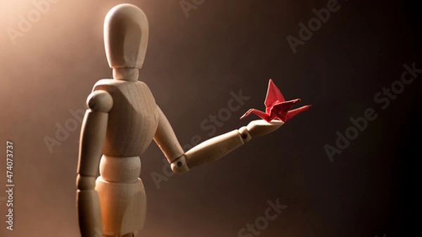 Fototapeta Big wooden mannequin holding red origami crane on his arm