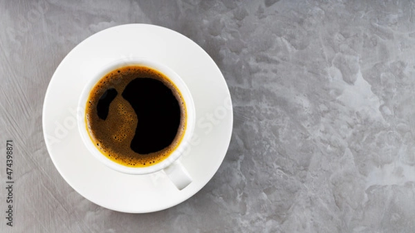 Fototapeta Cup of black coffee on a white saucer. Morning coffee in ceramic cup on a gray background. Top view. Copy space