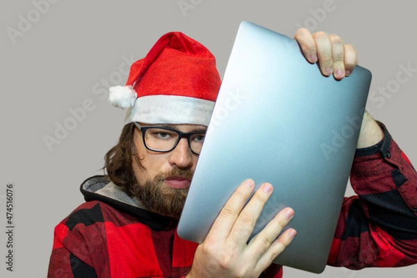 Fototapeta A man in a Santa hat with an aluminum laptop