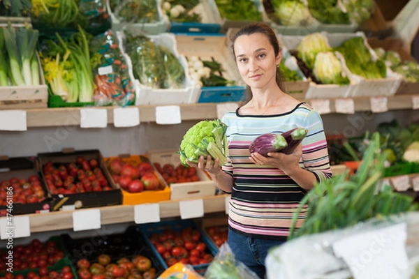 Fototapeta Positive Caucasian female choosing fresh broccoli at supermarket