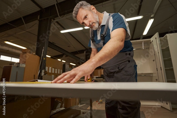 Fototapeta Serious grey-haired carpenter working in furniture manufacture