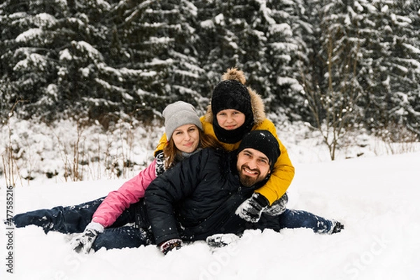 Fototapeta Happy family have fun in winter forest and looking at camera. Mother, father and son playing with snow. Family Christmas concept. Enjoying spending time together