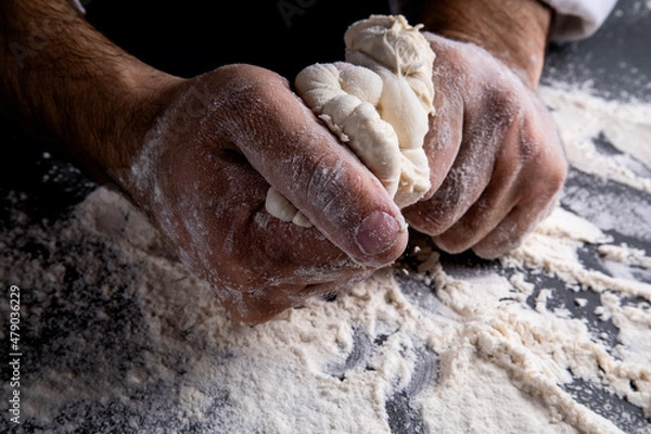 Fototapeta the chef kneads the dough on a dark background, the table is strewn with flour