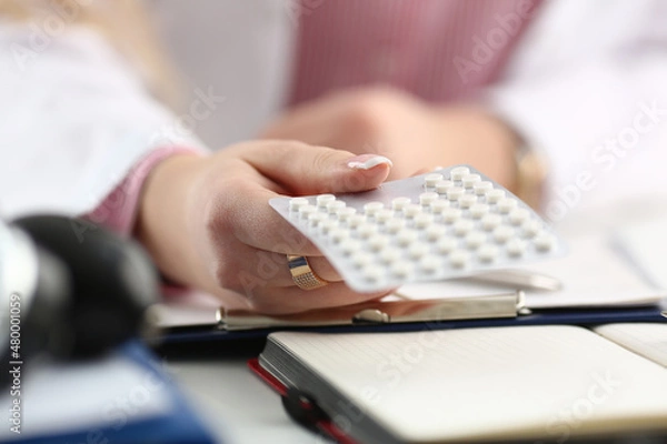 Fototapeta Doctor hand holding package of pills in workplace closeup