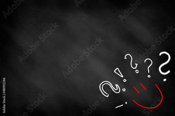 Fototapeta A happy face surrounded by exclamation marks and question marks drawn on a blackboard