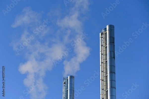 Fototapeta Steaming chimneys in the city. Concept for environment and industry. Background with blue sky.