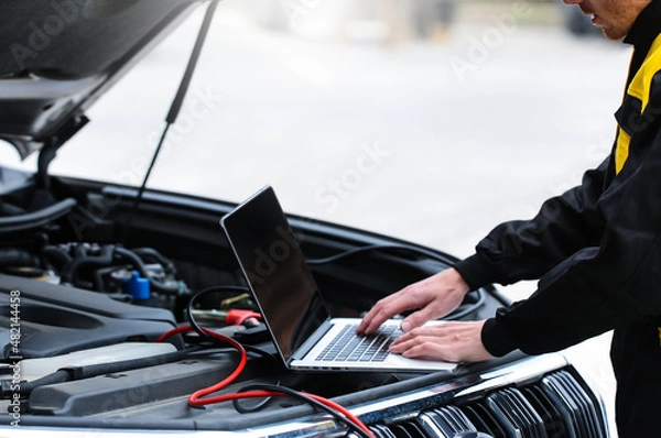 Fototapeta Mechanic using computer for diagnostics engine. Repairing car. Blur garage auto repair service in background.