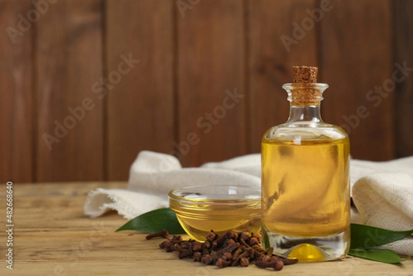 Fototapeta Essential oil and dried cloves on wooden table. Space for text