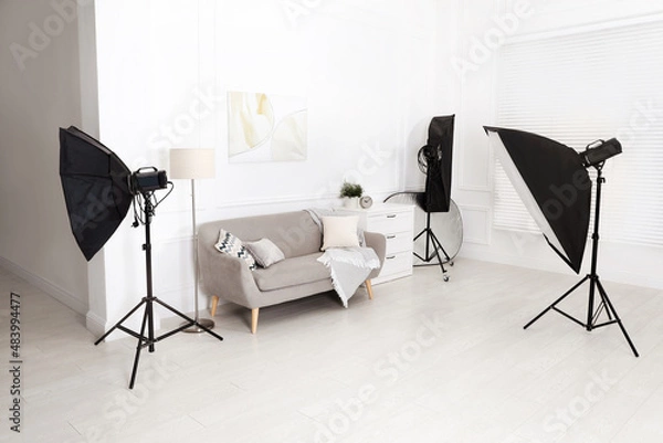 Fototapeta Set of stylish furniture surrounded by professional lighting equipment in photo studio. Cozy living room interior imitation