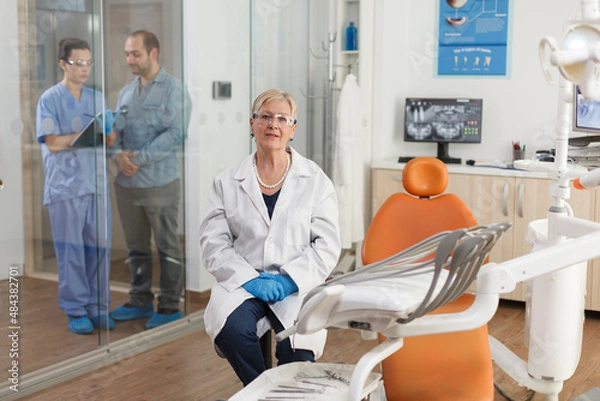 Fototapeta Portrait of stomatologist doctor looking into camera while waiting for patient during stomatology consultation in medical dental office. Orthodontist senior woman working at dentistry treatment