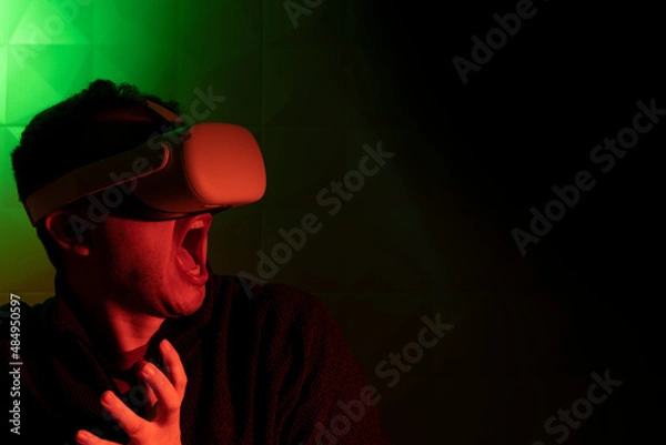 Fototapeta Man in white virtual reality goggles screaming in fear in red light