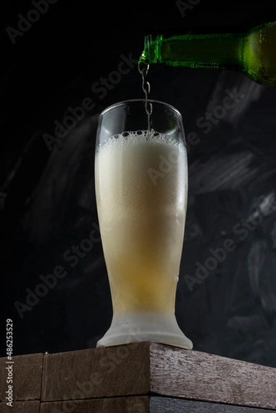 Fototapeta Beer pouring into cup in a bar. Wooden desk and grey background