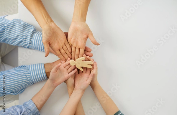 Fototapeta Happy young mum, dad and kids holding a little wooden toy figure of a child in their hands. Concept of family, adoption, love, care, protection, and safety. Top view close up, high angle closeup shot