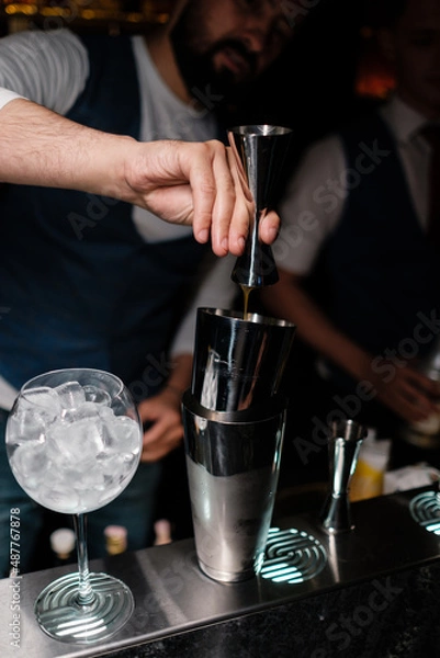 Fototapeta The bartender pours alcohol from a jigger into a shaker. A man learns how to make cocktails at the bar.