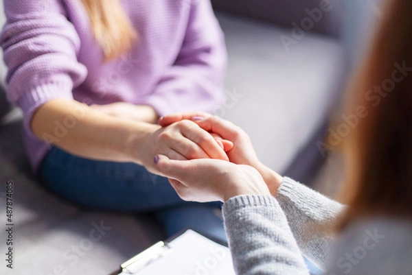 Fototapeta Close up of a female psychologist holding woman's hands during a therapy session. Psychotherapist supporting her depressed patient