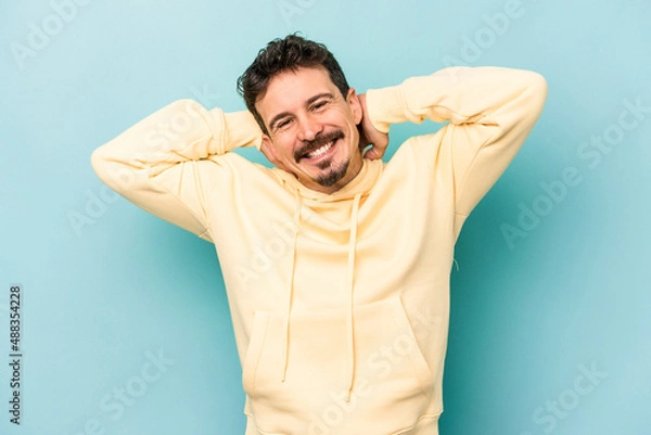 Fototapeta Young caucasian man isolated on blue background stretching arms, relaxed position.