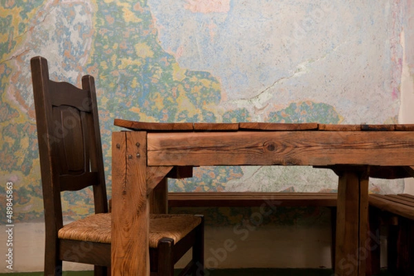 Fototapeta An old wooden table and chair. In the background is a colorful, cracked, dingy wall. Rustic interior.