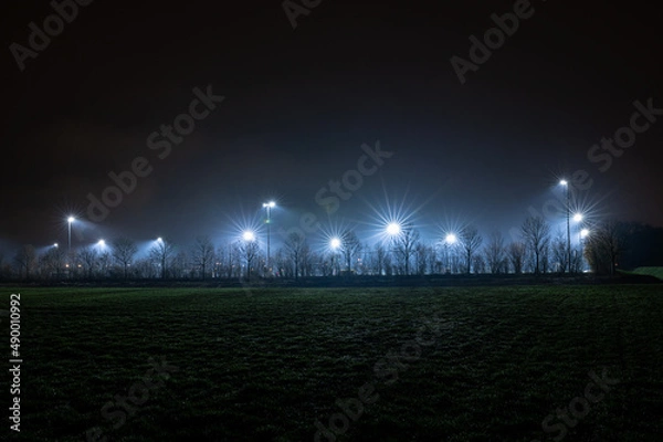 Fototapeta Light poles illuminate a sports field where training takes place in the evening