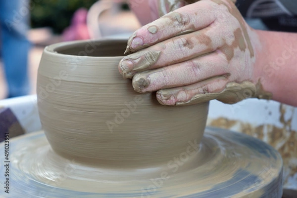 Fototapeta Close up hands working on pottery wheel and making a clay pot, selective focus