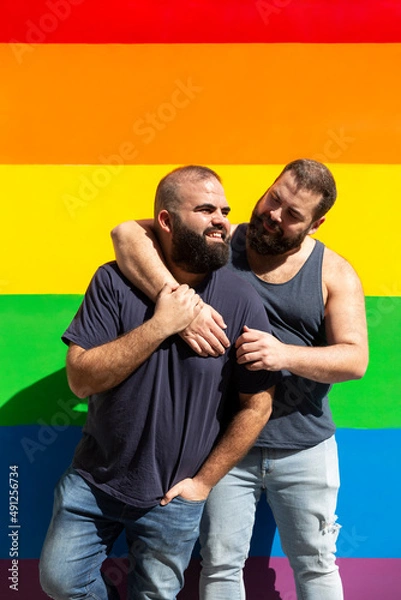 Obraz Young gay couple hugging on a background with rainbow colors. LGBT pride concept.