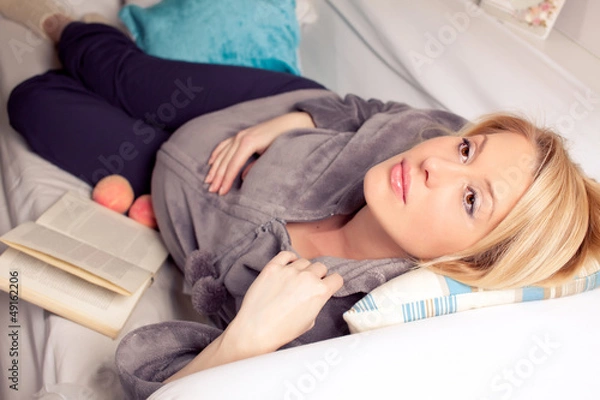 Fototapeta Pregnant blonde woman relaxing on sofa, reading book, dreaming,