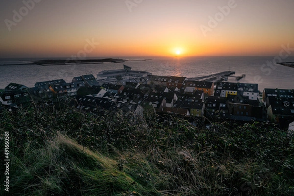 Fototapeta Sunrise above small port city of Helgoland, Germany. Sunrise colors in the sky. Sun disc rising on the distant horizon. Stair leading down to the city.