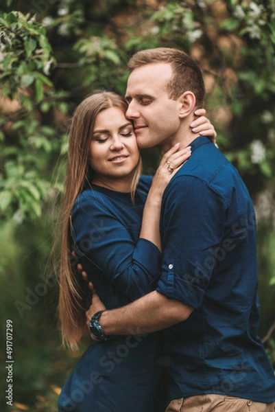 Fototapeta Handsome young guy with a girl stand in the spring garden. Romantic couple are walking in the park. Happy relationship concept