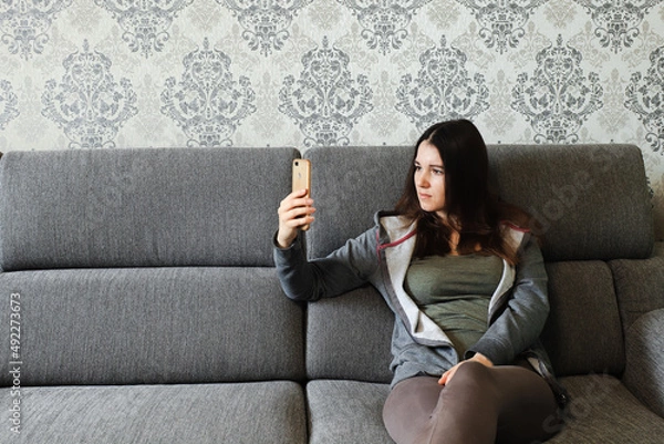 Fototapeta A woman is typing a text message on a smartphone, work from home, distant work. Photo of a young woman, communicating with followers using a mobile phone. Quarantined free time, copy space, banner