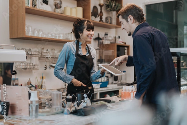 Fototapeta Caucasian woman barista take order from customer in coffee shop. female barista using digital tablet to take order. Coffee owner concept.