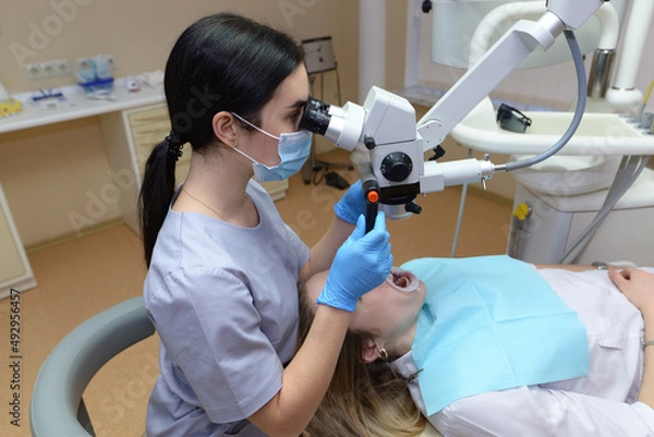 Fototapeta dentist examining a woman looking at her teeth with a professional microscope in a surgical dental office