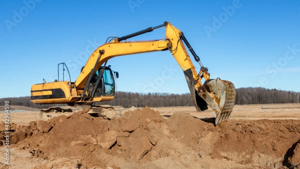 Fototapeta A powerful caterpillar excavator digs the ground against the blue sky. Earthworks with heavy equipment at the construction site.