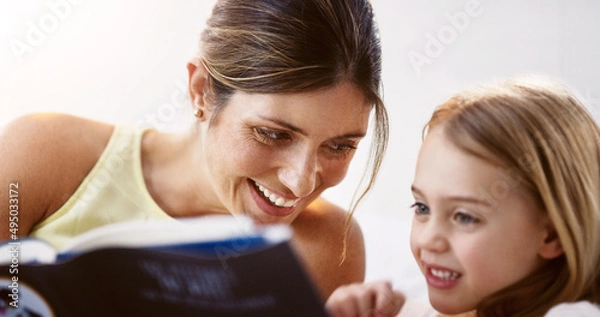 Fototapeta We share a similar love for books. Shot of a beautiful young mother reading a book with her daughter at home.